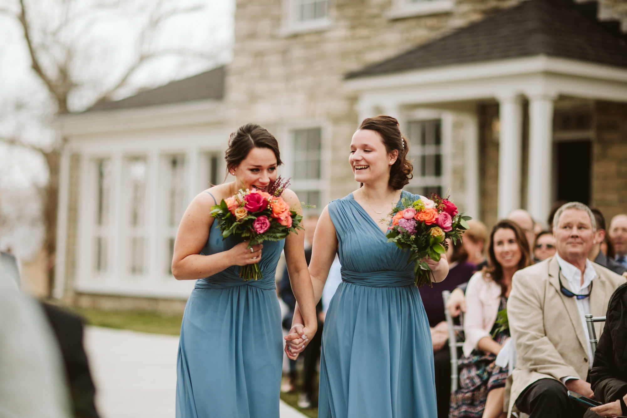 Bridesmaids, the bride's sisters, tearing up as they walk down the aisle at the stone house of st charles