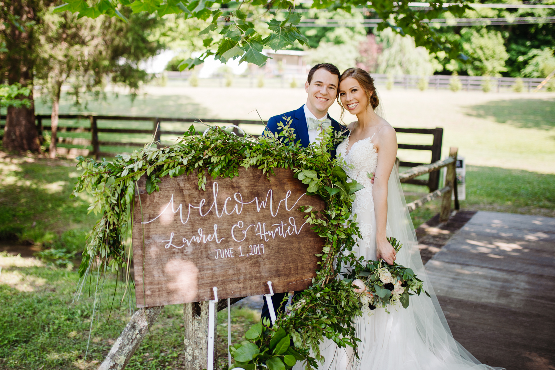 bride and groom with their hand-lettered welcome sign at a stables at strawberry creek wedding in Knoxville, tennessee